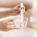 Hand holding a white xiaomi TDS water tester dipped in a glass cup, measuring water purity with a digital display 