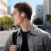 A young man with a backpack on a Close-up of a man wearing a white soundcore V20i open-ear earbud while walking outside.
