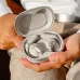 Handheld view of JBL Sense Pro earbuds in light gray case with logo inside lid, emphasizing portability and style.