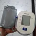 Close‑up of a hand holding Omron HEM‑7140T1 BP Monitor with attached cuff and visible START/STOP button.
