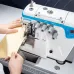 Close-up of a person feeding yellow fabric into the Jack E4S-5-03/333 overlock machine with visible thread cones and ruler markings.