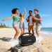 Beach lifestyle view of Unikyy Vigor 50W Portable Bluetooth Speaker placed on sand with people nearby highlighting outdoor portability