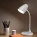 White desk lamp lighting an open book on a wooden desk in a dim room.