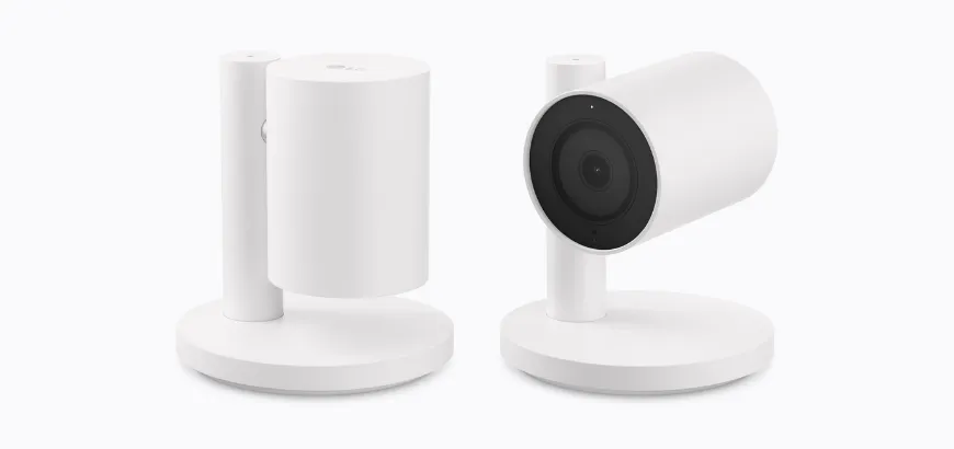 Three-quarter view of two white LG Indoor Cam Plug-In desktop security cameras on circular stands, showing side and front angles.
